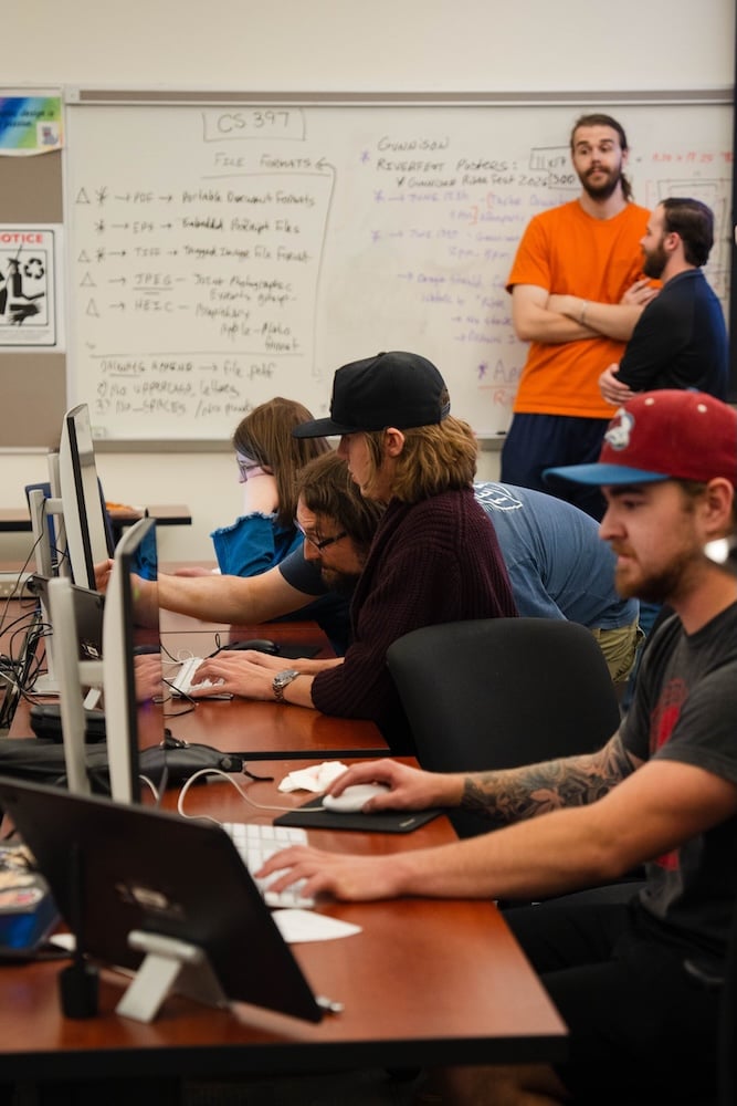 A Western student recieving computer help from a mentor in a computer room full of people.