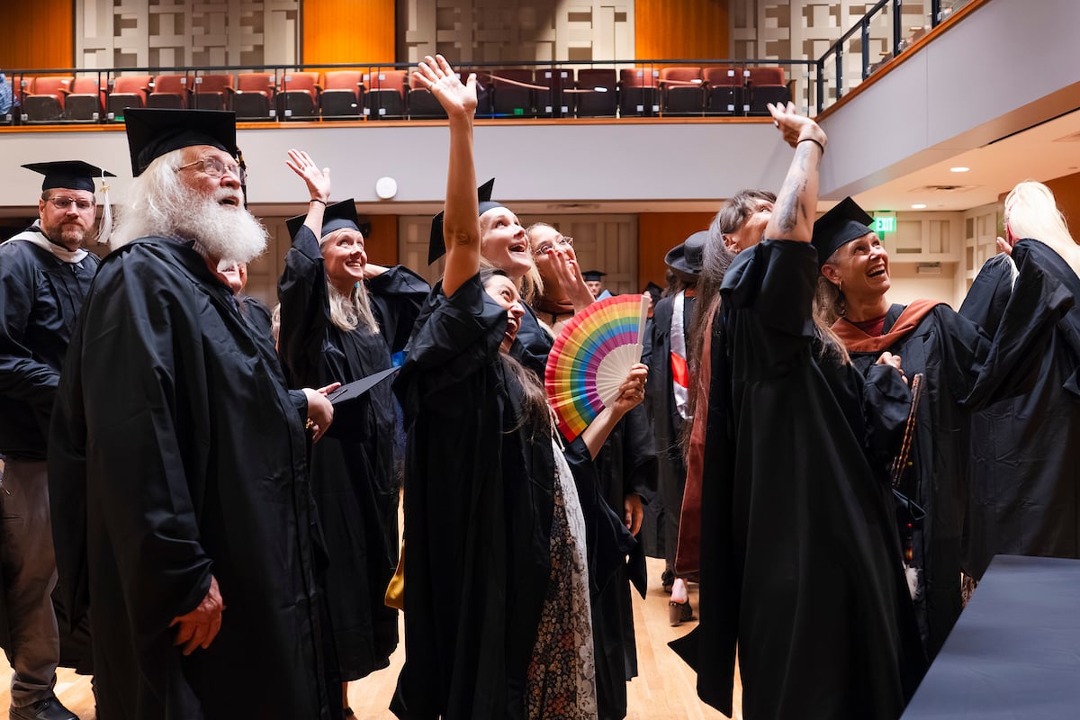 A group of poetry students all wave at someone sitting in the upper level of Kincaid Concert Hall after the Graduate Program in Creative Writing's commencement ceremony.