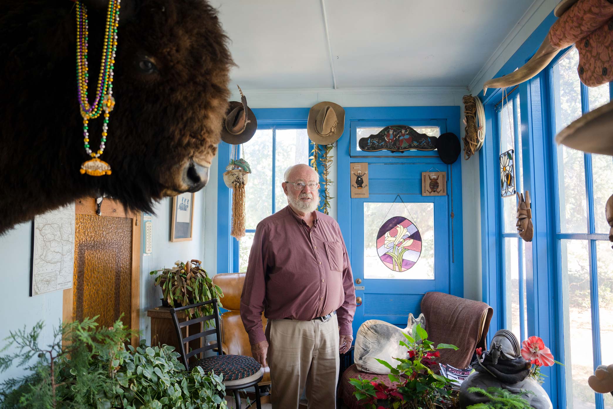 A photo of Butch Clark standing in one of the rooms of his house that has many windows and a large bison head mounted on the wall.
