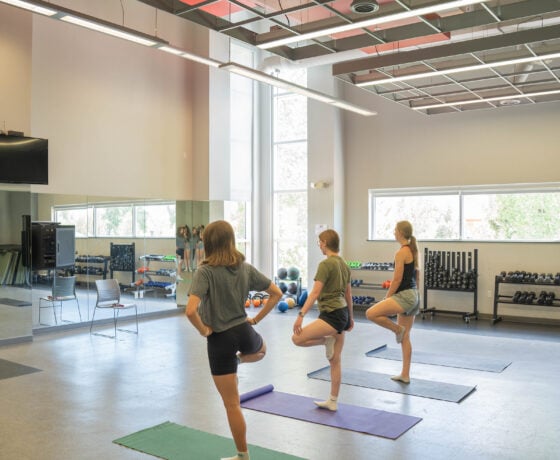 3 female students doing yoga in a fitness room.