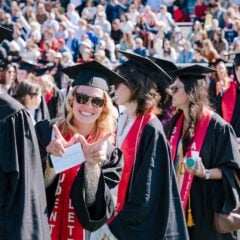 In a crowd of people, a graduate holds up a W with her hands.