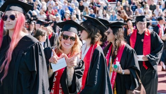 In a crowd of people, a graduate holds up a W with her hands.