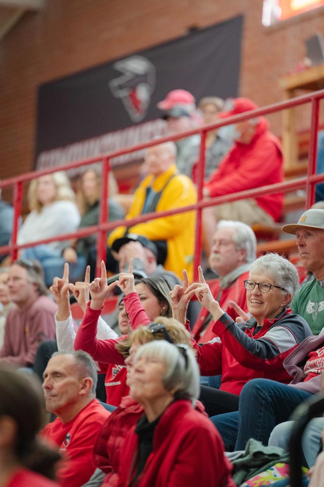 Three Western basketball fans hold up Ws with their hands during a free throw while sitting in the stands during a women's basketball game.