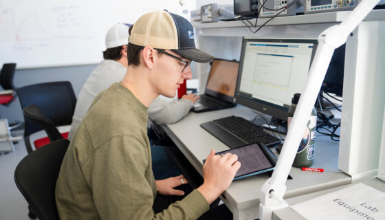 An engineering student works on a program on on an iPad and computer.