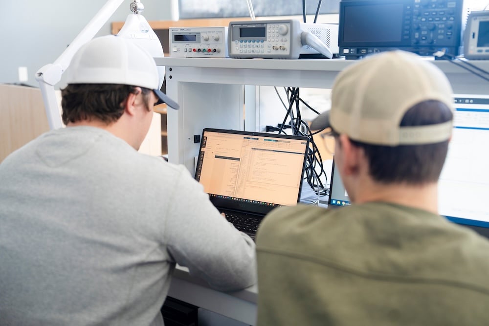 Two engineering students work together with some progams and graphs between two computers and an iPad.