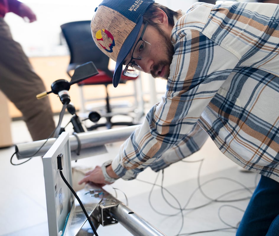 An engineering student feeds a wire down the metal pipe of the sensor suite he's helping build for the Rocky Mountain Biological Laboratory.