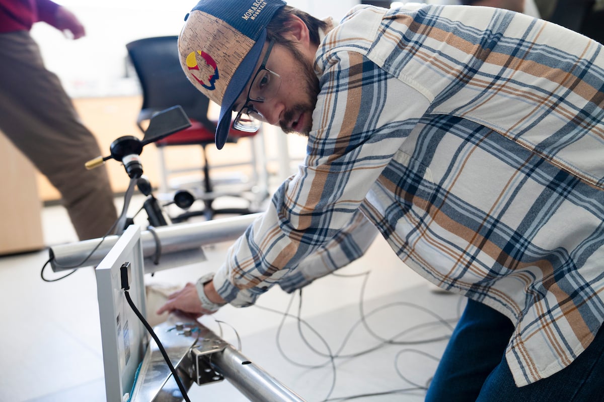 An engineering student feeds a wire down the metal pipe of the sensor suite he's helping build for the Rocky Mountain Biological Laboratory.