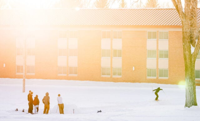 Students session a PVC pipe on campus after a fresh snow during golden hour.