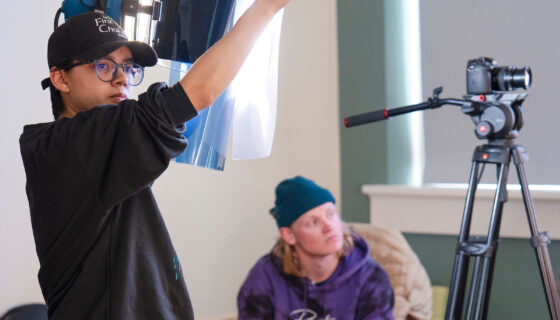 A student holds a diffuser over a light during a color correction demonstration for a film class.