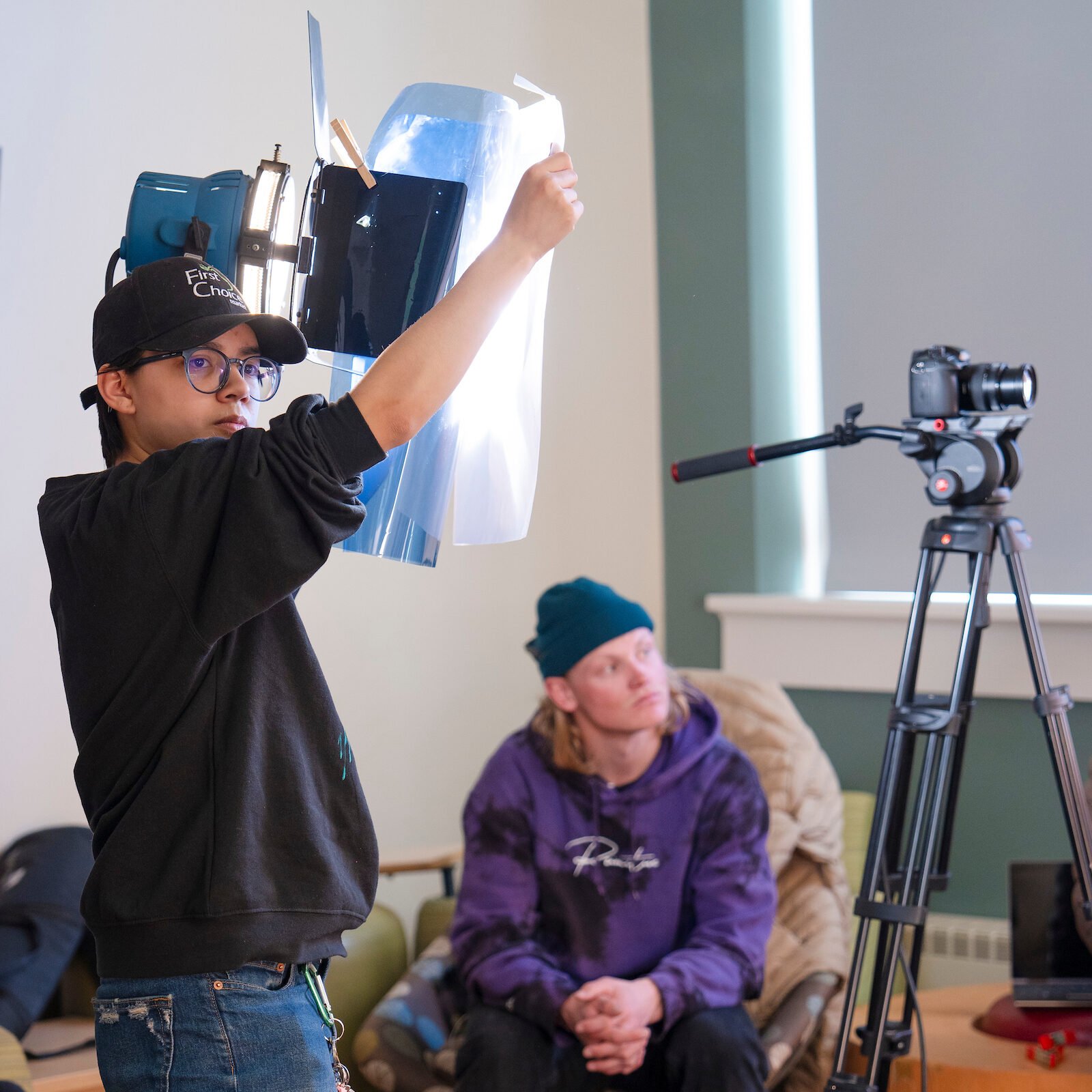 A student holds a diffuser over a light during a color correction demonstration for a film class.