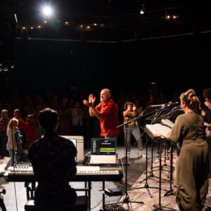 Steven Cole Hughes stands in the middle of the studio theatre and joins the audience in clapping for the cast after their performance of his musical 'Singletrack!'.