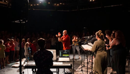 Steven Cole Hughes stands in the middle of the studio theatre and joins the audience in clapping for the cast after their performance of his musical 'Singletrack!'.