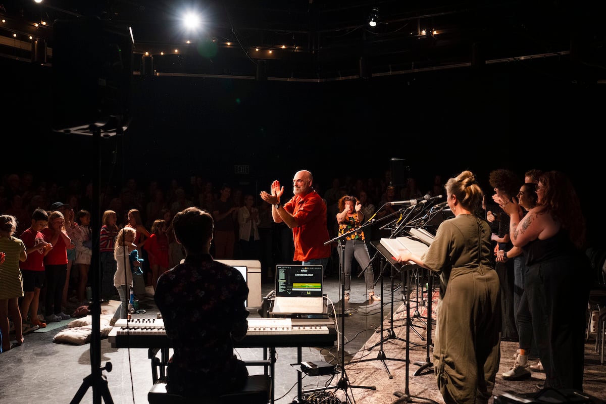 Steven Cole Hughes stands in the middle of the studio theatre and joins the audience in clapping for the cast after their performance of his musical 'Singletrack!'.