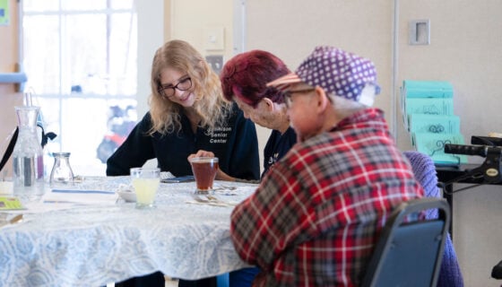 Rural Health MBS student Maddie Gregurek looks at images on a woman's phone and listens to her talk during a lunch at the Senior Center.