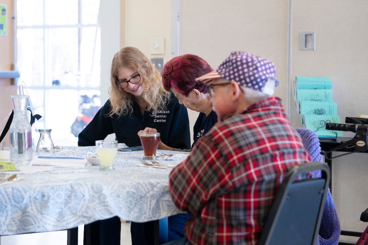 Rural Health MBS student Maddie Gregurek looks at images on a woman's phone and listens to her talk during a lunch at the Senior Center.