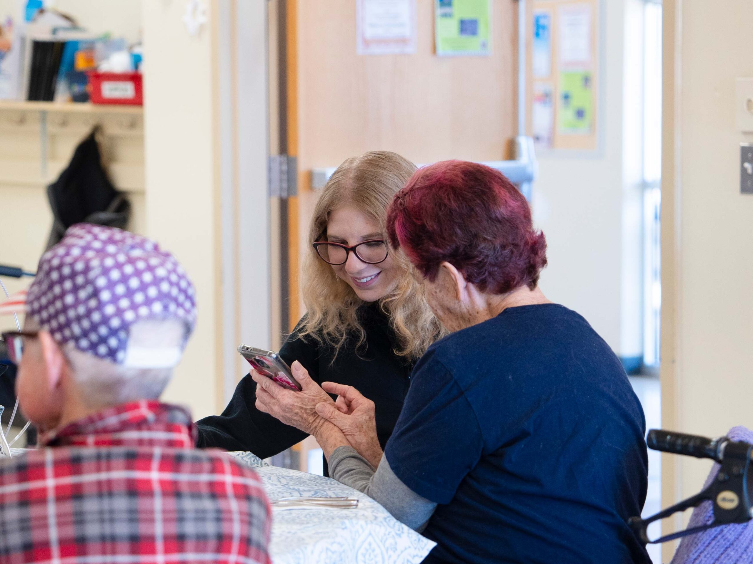 Rural Health MBS student Maddie Gregurek looks at images on a woman's phone and listens to her talk during a lunch at the Senior Center.