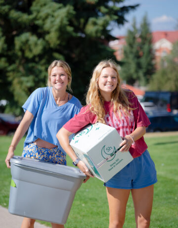 First-year students smile while holding boxes during move in