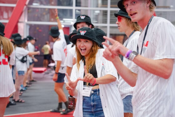 An orientation leader smiles with her hands in the shape of a "w"