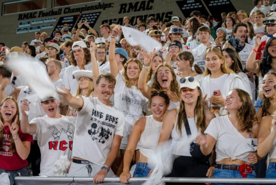 Student section celebrates after touchdown with smiles and hands in the air waving Mountaineer towels.