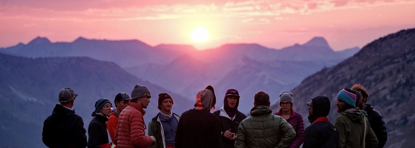 A group of students stand on a mountain ridge at sunrise.
