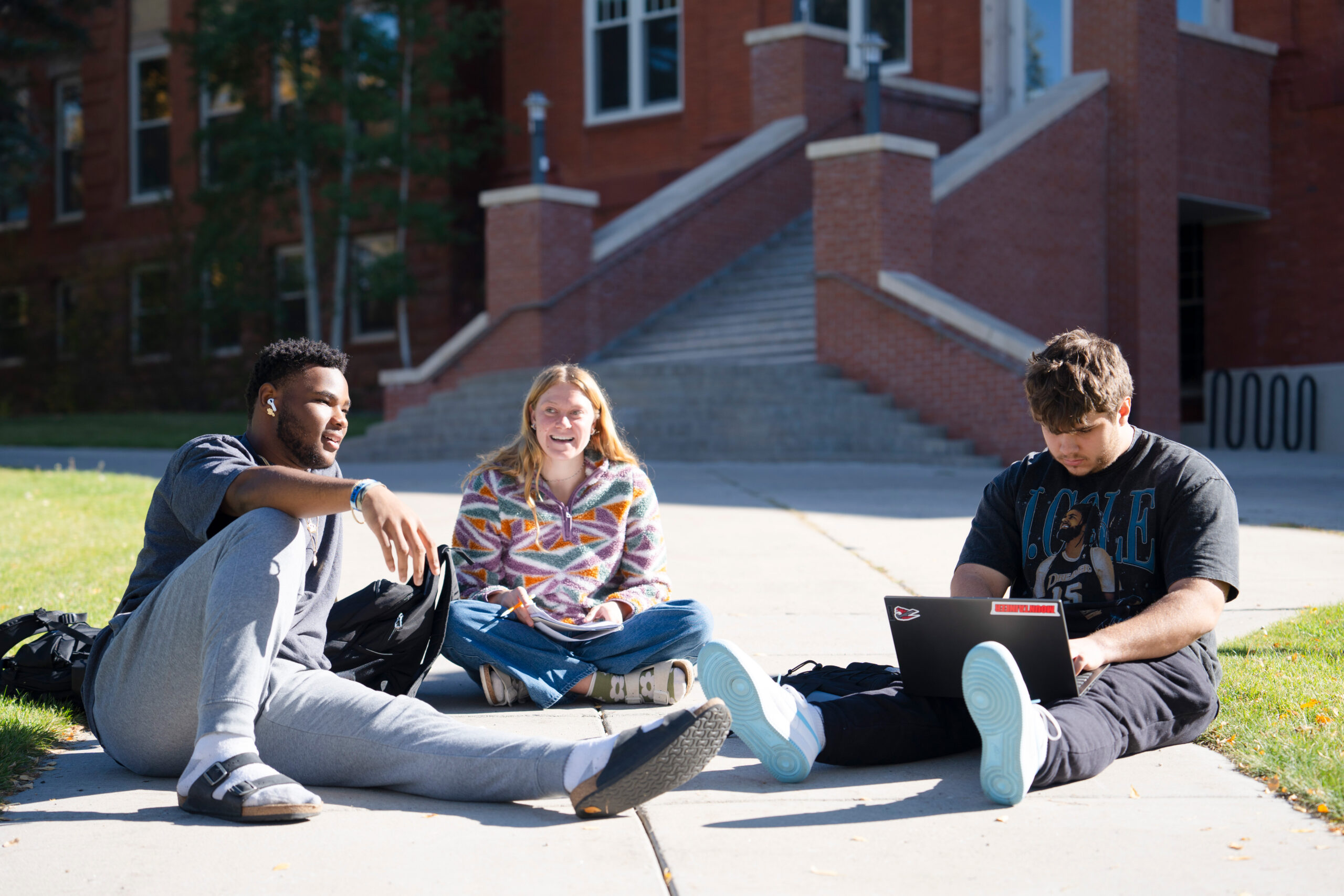 A group of three students sit on Taylor Lawn and discuss an assignment for a philosophy class.