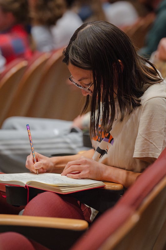 Female student takes notes on the issues the keynote speaker and panelists talk about in agriculture in Colorado