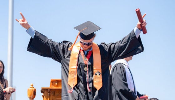 A male graduate from the Rady School of Engineering walks down the stage stairs with his hands in the air, celebrating graduation.