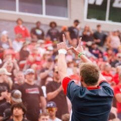 A cheerleader holds his hands in the shape of a W while cheering to the crowd during a football game.