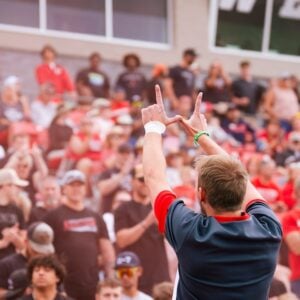 A cheerleader holds his hands in the shape of a W while cheering to the crowd during a football game.