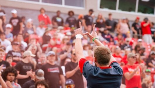 A cheerleader holds his hands in the shape of a W while cheering to the crowd during a football game.