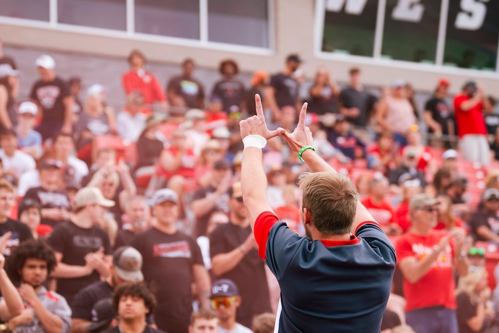 A cheerleader holds his hands in the shape of a W while cheering to the crowd during a football game.