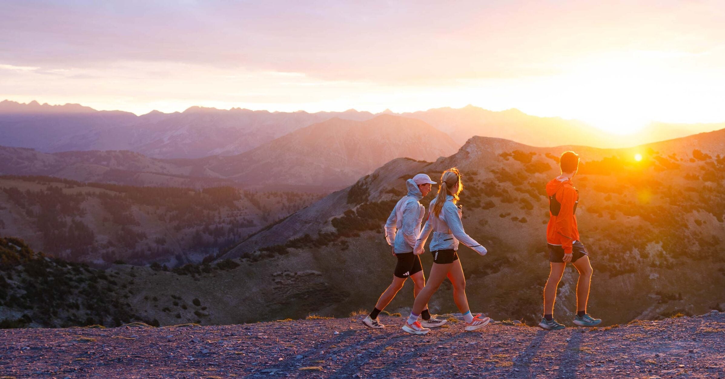 Three trail runners walk an alpine ridge at sunrise.