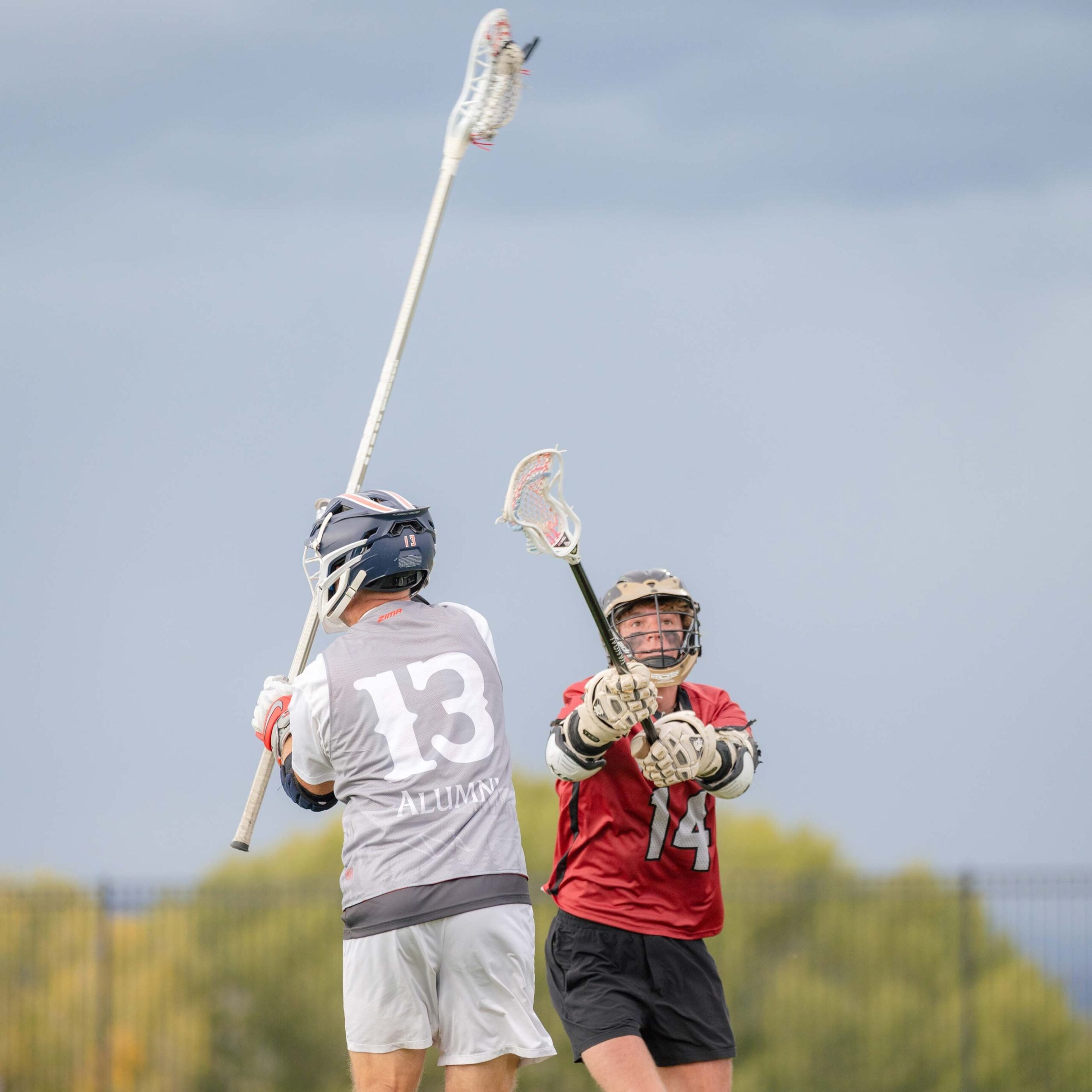 Current western player attempts to block alumn's stick from throwing the ball