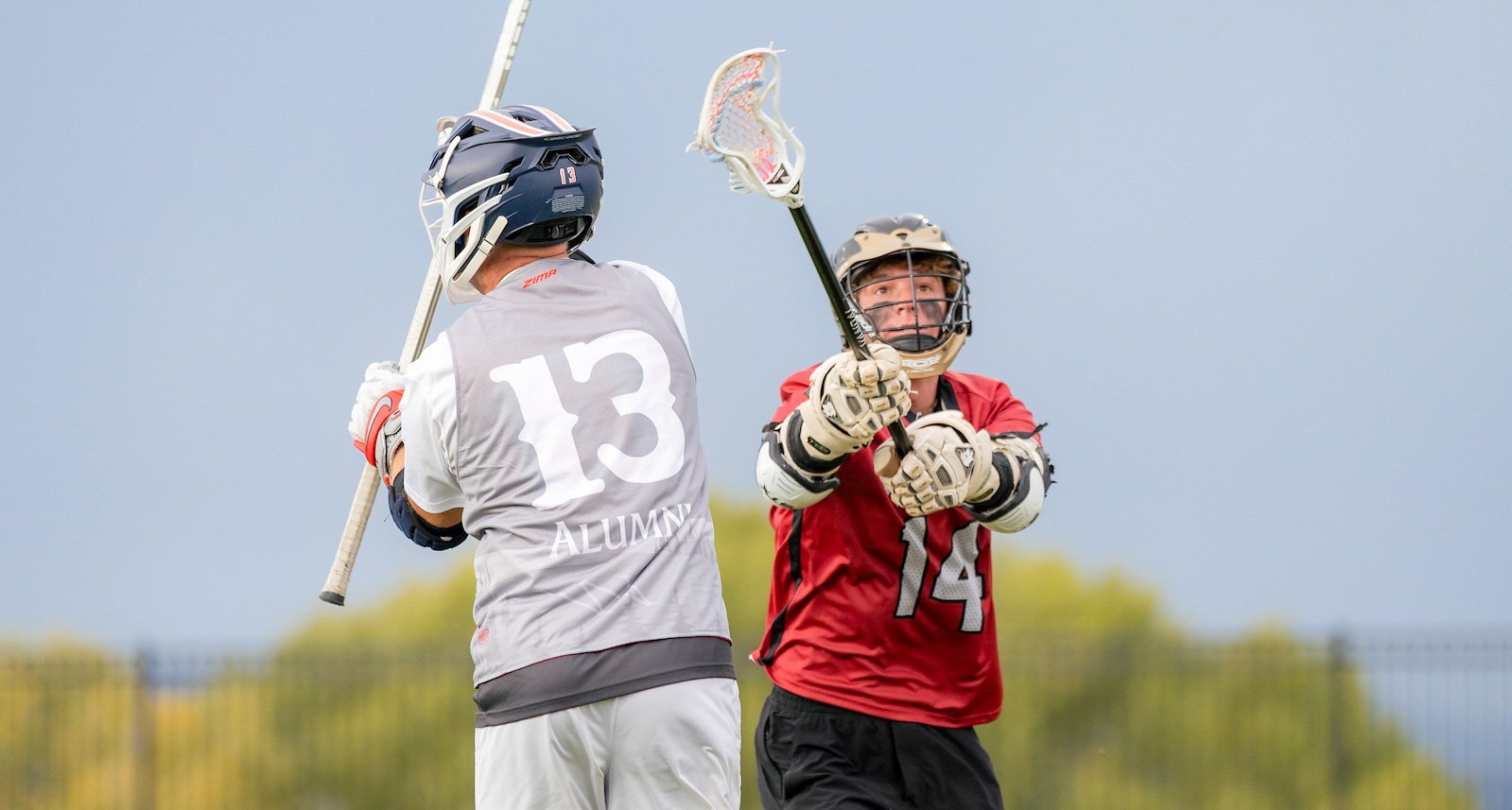 A Western lacrosse athlete attempts to block an alumni's stick from throwing the ball.