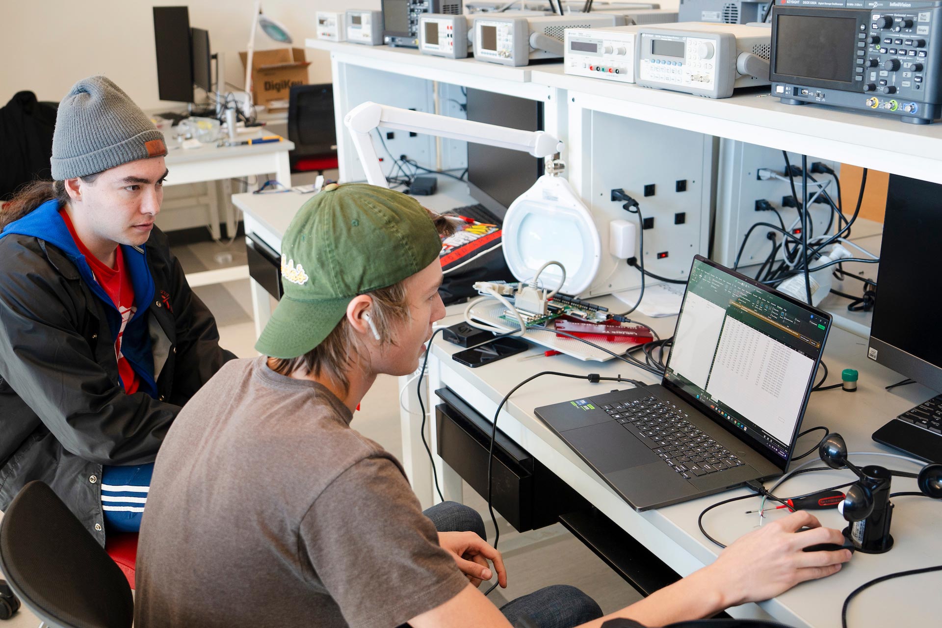 Two engineering students look at the screen of a laptop while assembling a sensory suite for the Rocky Mountain Biological Lab.