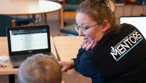 A Western student teacher works with a student on a laptop.