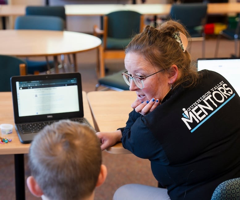 A Western student teacher works with a student on a laptop.