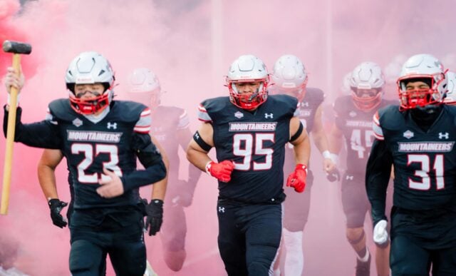Football athletes run onto the field through pink smoke.