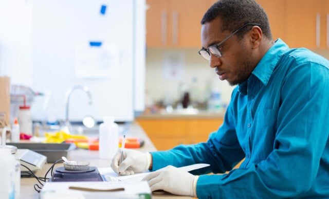 Etinosa Igunbor writes observations in a notebook while working with soil samples for his Master's in Environmental Management graduate project.