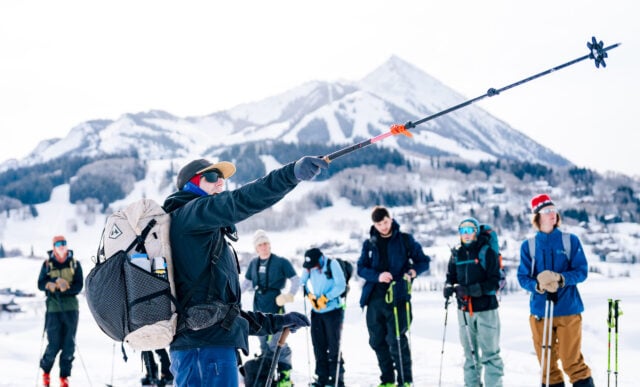 Professor Dave Erbe points his ski pole uphill in front of his backcountry skiing class. Mount Crested Butte is seen in the background.