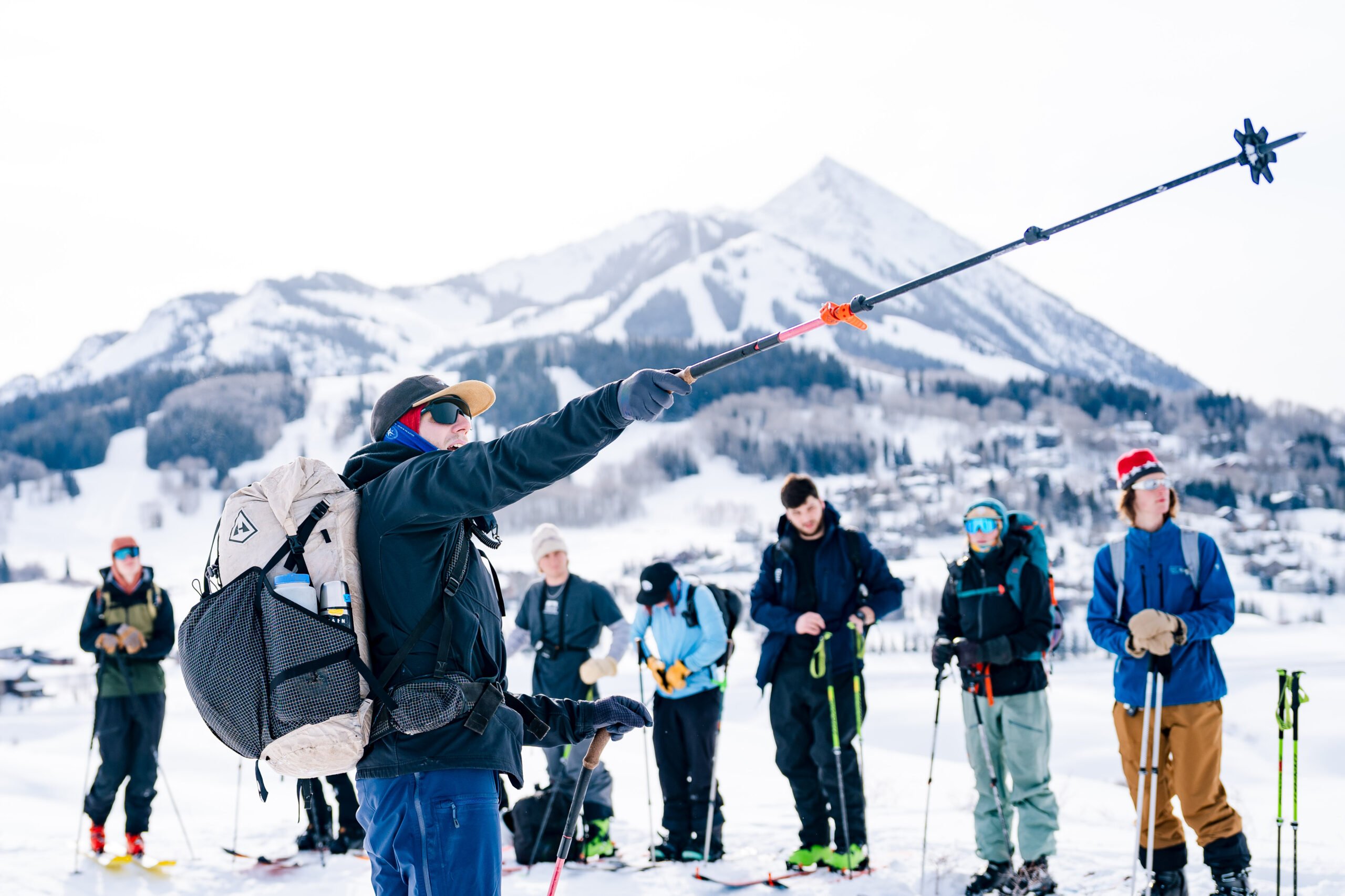 Professor Dave Erbe points his ski pole uphill in front of his backcountry skiing class. Mount Crested Butte is seen in the background.