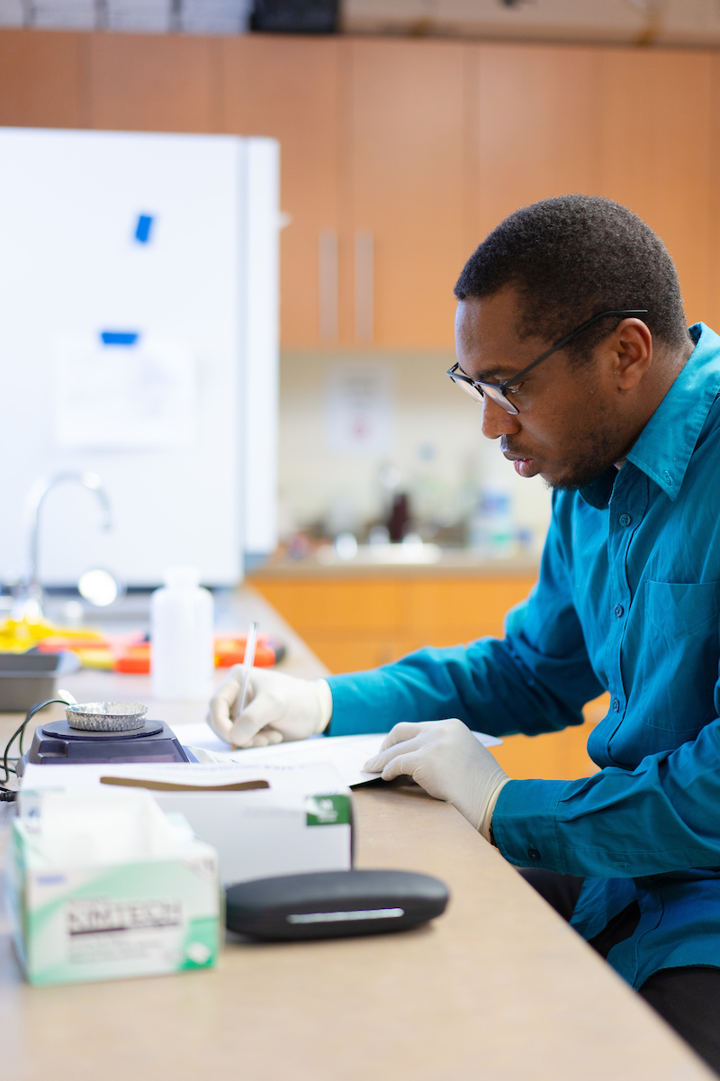 Etinosa Igunbor writes observations in a notebook while working with soil samples for his Master's in Environmental Management graduate project.