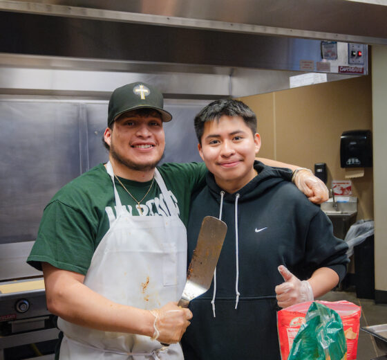 Two students in the Amigos club smile for a photo in a kitchen while making tostadas.