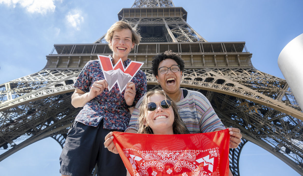 Photo of three students smiling below the Eiffel Tower, one holding a cut-out of Western's W logo.