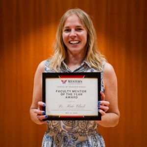 Dr. Kate Clark smiles while holding her Faculty Mentor of the Year award at the 2026 Distinguished Achievement in Graduate Studies ceremony.