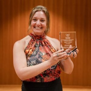 Natalie Pax holds up her glass award at the 2026 Distinguished Achievement in Graduate Studies ceremony.