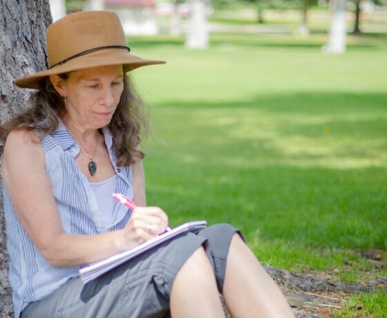 A creative writing student sits under a tree on Taylor Lawn and writes in her journal