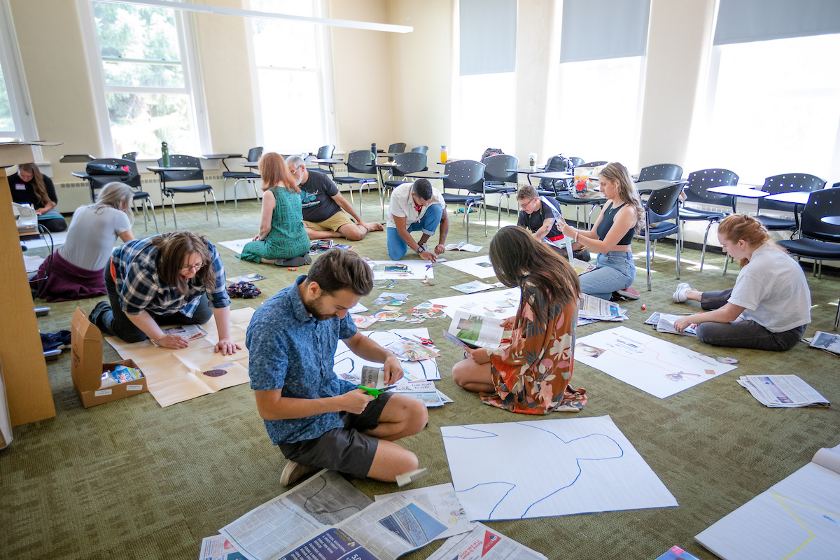 Students are scattered on the floor of a classroom working on collage posters during the GPCW summer residency