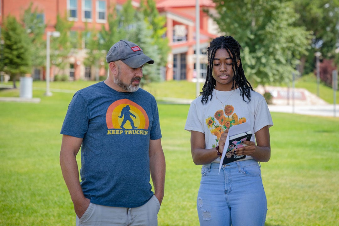 A screenwriting student checks his script with the director of the short film they are making in class on the lawn outside of the Welcome Center