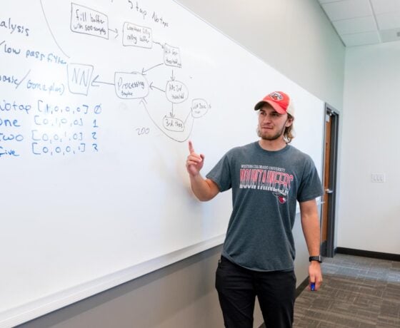 A student points at an equation on a whiteboard.